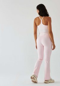 Jasnoróżowy strój sportowy składający się z dopasowanego topu na ramiączkach z tyłem typu racerback oraz rozkloszowanych legginsów, wykonany z gładkiego, rozciągliwego materiału.