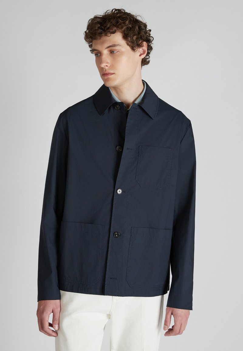 Granatowa, lekka kurtka z wyraźnym kołnierzem, dwiema przednimi kieszeniami i jedną kieszenią na klatce piersiowej. Gładka tekstura i guziki z przodu.