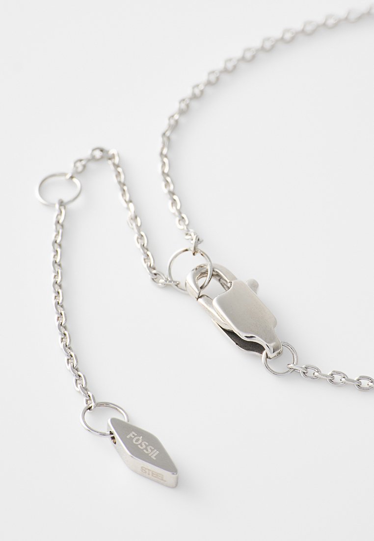 Zilveren ketting met een kreeftenhaak en een klein label gegraveerd met "Fossil Steel" op een witte achtergrond.