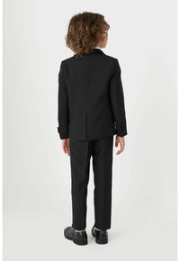 Un costume noir composé d'une veste ajustée et d'un pantalon assorti. La veste présente un col cranté et des poignets à bouton.