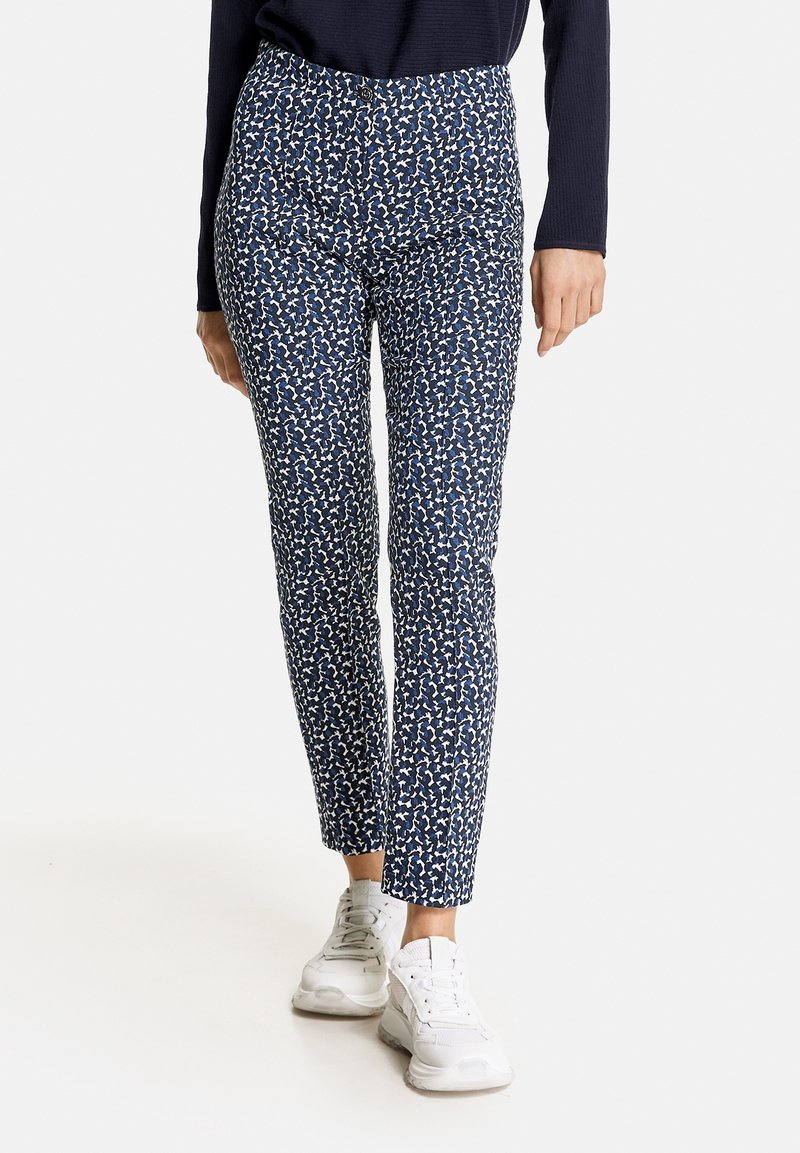 Pantalon bleu marine avec un motif abstrait blanc intégral. Coupe ajustée avec une texture lisse. Associé à des baskets blanches.