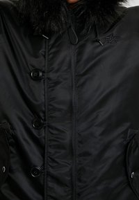 Czarna pikowana kurtka z kapturem wykończonym futerkiem, z zamkiem błyskawicznym z przodu, dwoma dużymi bocznymi kieszeniami i czterema guzikami jako ozdobą.