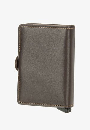 Cartera compacta de cuero marrón oscuro con costuras visibles y una pequeña pestaña negra de plástico en la esquina inferior.