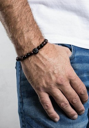 Beaded bracelet featuring dark red and black stones, with a textured black centerpiece, worn on a hand against denim fabric.
