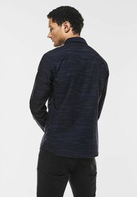 Námořnická košile s dlouhým rukávem a vertikálním pruhovaným vzorem, obsahující límec a manžety na knoflíky. Materiál se zdá být měkký s texturovaným povrchem.