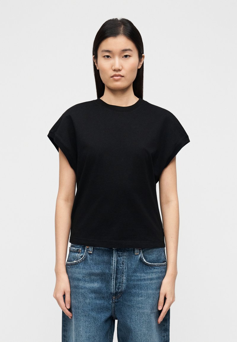 Μαύρο βαμβακερό μπλουζάκι με κοντά, γυριστά μανί�κια και στρογγυλή λαιμόκοψη, σε συνδυασμό με ανοιχτό μπλε, φαρδιά τζιν παντελόνια.