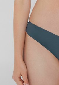 Czarne bikini dolne o gładkiej fakturze, minimalnym pokryciu i prostym designie. Zbliżenie ukazujące pasek i karnację skóry.