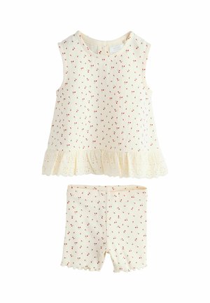 Světle krémový dvoudílný outfit s tílkem bez rukávů s červeným potiskem třešní a krajkovým lemem, doplněný o kraťasy se stejným třešňovým potiskem.