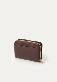 Portofel din piele burgundy cu fermoar auriu, de formă rectangulară și cu o suprafață texturată; are un slot extern pentru carduri și un charm decorativ.