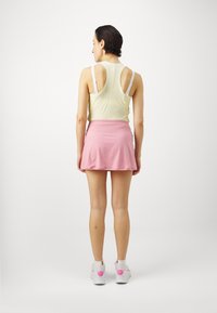 Sportoutfit mit einem hellgelben ärmellosen Oberteil und einem rosa ausgestellten Rock, kombiniert mit weißen Schuhen mit pinken Akzenten.
