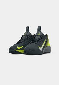 Sorte og neongrønne Nike træningssko med hvide og gule swooshes, sorte snørebånd og trækflige på en hvid baggrund.