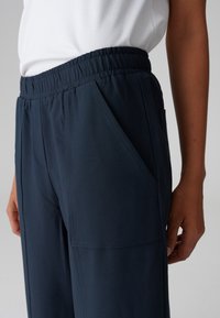 Pantalons en tissu extensible bleu marine avec une taille élastique, des poches latérales et une coupe droite, présentant des coutures nettes et une texture lisse.