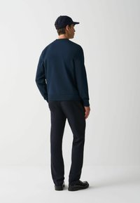 Marineblauwe sweatshirt en broek, beide van een zachte stof. De sweatshirt heeft een geribbelde halslijn en manchetten, gecombineerd met elegante zwarte schoenen.