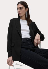 Svart skräddarsydd kavaj av slättyg, med spetsig slag, kombinerad med en vit t-shirt och högmidjade svarta jeans.
