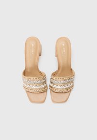 Sandales à talon bloc beige avec des brides décoratives tressées ornées de fils dorés et bleus, en cuir lisse et avec un design à bout carré.