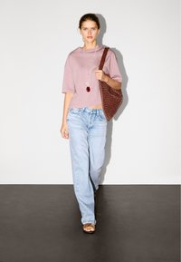 Hellrosa, kurz geschnittenes T-Shirt, lockere, hellblaue Jeans, braune geflochtene Schultertasche und braune Sandalen mit Riemen. Minimalistisches Design, lässiger Stil.