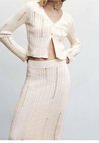 Zweiteiliges Strickset in sanftem Beige, bestehend aus einer kurzen Strickjacke mit Knopfverschluss und einem hochtaillierten Rock, beide mit strukturierten Mustern.