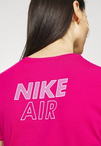 Růžové bavlněné tričko s textem "NIKE AIR" na zadní straně v bílé barvě s texturovaným vzorem, krátkými rukávy a kulatým výstřihem.