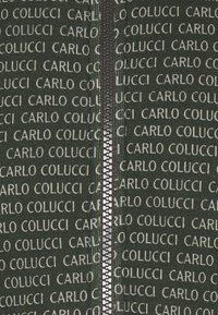 Zelená zipová bunda se opakujícím se bílým textem "CARLO COLUCCI" a stříbrným zipem, která se pyšní hladkou texturou látky.