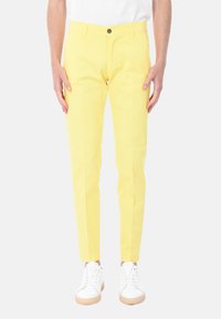 Pantaloni gialli in cotone con una vestibilità slim, dotati di tasche frontali, chiusura con bottone e una texture sottile. Abbinati a sneakers bianche.