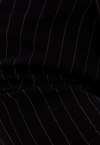 Svart tyg med vertikala vita pivotter. Materialet har en strukturerad väv som framhäver en skräddarsydd finish.