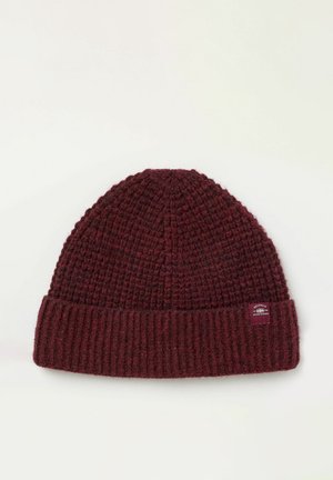 Gorro de punto color burdeos con el borde vuelto de canalé y una pequeña etiqueta de marca, colocado sobre un fondo blanco.