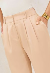 Beige plooibroek gemaakt van een gladde stof, met een brede tailleband en zijzakken, met een slanke, getailleerde pasvorm.