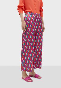 Färgglada vida byxor med ett geometriskt mönster i rosa, röd och teal. Tillverkade av ett lätt material med en mjuk yta.