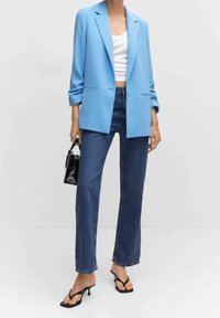 Vaaleansininen bleiseri, valkoinen toppi, tummansiniset suoralahkeiset farkut. Asun täydentävät musta käsilaukku ja varvassandaalit. Sileä kangas, räätälöity malli.