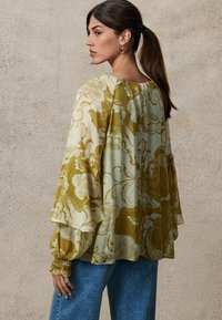 Bluză florală cu mâneci evazate, în nuanțe de verde măsliniu și crem, realizată dintr-un material ușor, cu manșete gathered și o croială lejeră.
