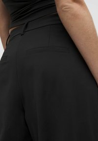 Pantaloni neri in tessuto liscio, con un taglio comodo, tasche posteriori con cuciture minime e dettaglio del cordoncino in vita.