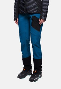 Blauwe technische broek met een zwarte zak, taps toelopende pijpen en verstevigde manchetten. Gemaakt om te dragen met zwarte laarzen, geschikt voor outdoor activiteiten.