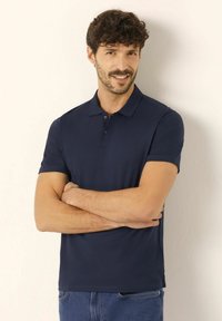 Marinblå pikétröja i slät bomullstyg, med krage, treknappslås och korta ärmar, matchad med avslappnade denimjeans.