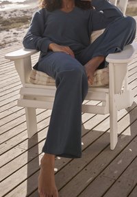 Granatowy, prążkowany zestaw odzieży domowej składający się z luźnej bluzki z dekoltem w kształcie V oraz spodni prostych nóg, noszony podczas siedzenia na białym, drewnianym krześle.