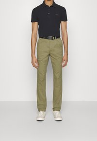 Marineblauw poloshirt met een klein logo op de borst, gecombineerd met kaki chino's en een zwarte riem. De schoenen zijn licht van kleur met witte veters.