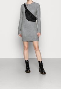 Robe en maille grise à manches longues, associée à un sac bandoulière noir et des bottes de combat noires à lacets. Texture lisse, coupe ajustée.