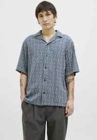 Camisa de manga corta abotonada de color azul con un patrón de diamantes. Fabricada en tejido ligero, cuenta con un corte holgado y cuello.