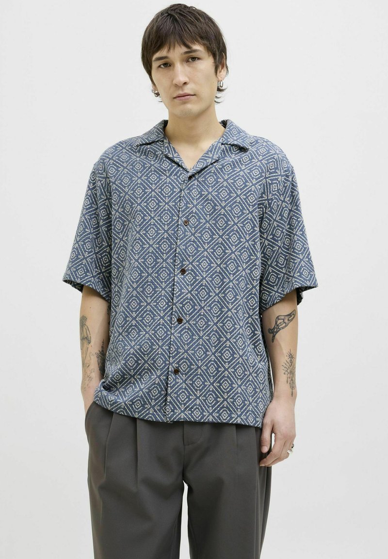 Camisa de manga corta abotonada de color azul con un patrón de diamantes. Fabricada en tejido ligero, cuenta con un corte holgado y cuello.