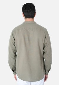 Camicia verde oliva a maniche lunghe con orlo dritto, tessuto leggero e polsini con bottoni. Presenta un design semplice con un dettaglio a yoke sul retro.