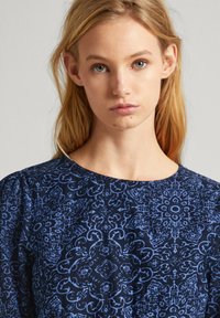 Námornícky modrý top s kvetinovým a paisley vzorom, okrúhlym výstrihom a naberanými rukávmi, vyrobený z ľahkého materiálu s hladkým povrchom.