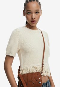 Strikket creme kortærmet sweater med frynset kant, parret med en brun læder crossover-taske med nitter og syede mønstre.