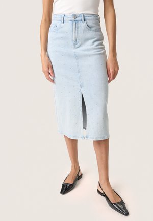 Jasnoniebieska midi spódnica jeansowa w drobne kropki z rozcięciem z przodu, noszona z czarnymi czółenkami typu slingback z ostrym noskiem.