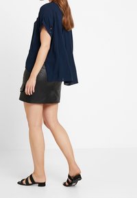 Blusa blu navy a maniche corte, morbida e comoda, abbinata a una minigonna in pelle nera e a sandali neri senza tacco. Design e texture semplici.