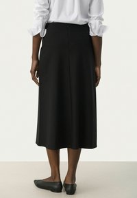 Gonna nera fino al ginocchio con una texture liscia, chiusura con zip laterale e una sottile forma a campana. Abbinata a una camicia bianca con maniche lunghe.