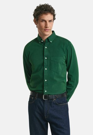 Groene overhemdd met lange mouwen, gemaakt van katoen, met een borstzak en witte knopen, gecombineerd met donkerblauwe spijkerbroek en een zwarte riem.
