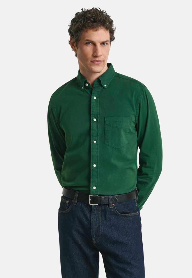 Groene overhemdd met lange mouwen, gemaakt van katoen, met een borstzak en witte knopen, gecombineerd met donkerblauwe spijkerbroek en een zwarte riem.