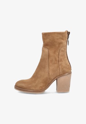 Bottine en daim beige à talon bloc, bout arrondi, fermeture éclair latérale et détails surpiqués le long de la semelle et des côtés.