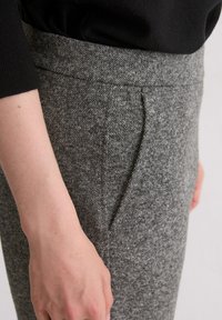 Graue, strukturierte Hose mit geradem Schnitt, ausgestattet mit einer dezenten Seitentasche und einem glatten Bund. Das Material wirkt weich und leicht.