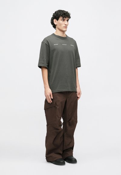 Maslinasto zelena oversized majica s kratkim rukavima i tekstualnim detaljima, u kombinaciji s smešnim cargo hlačama koje imaju džepove i ležeran kroj.