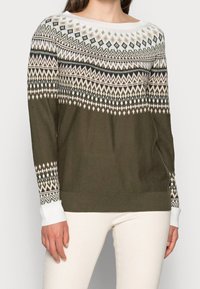 Pull vert olive à encolure ronde, motif tricoté avec des motifs géométriques blancs et noirs sur les manches, et poignets côtelés.